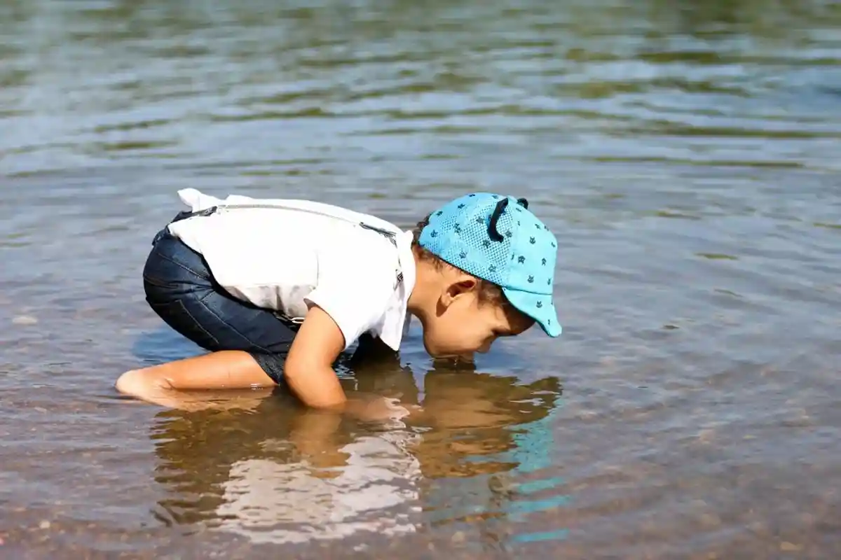 Little boy drinking water from the river