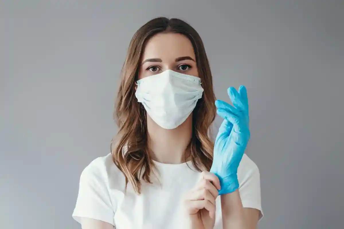 Женщина в медицинской маске одевает перчатку фото