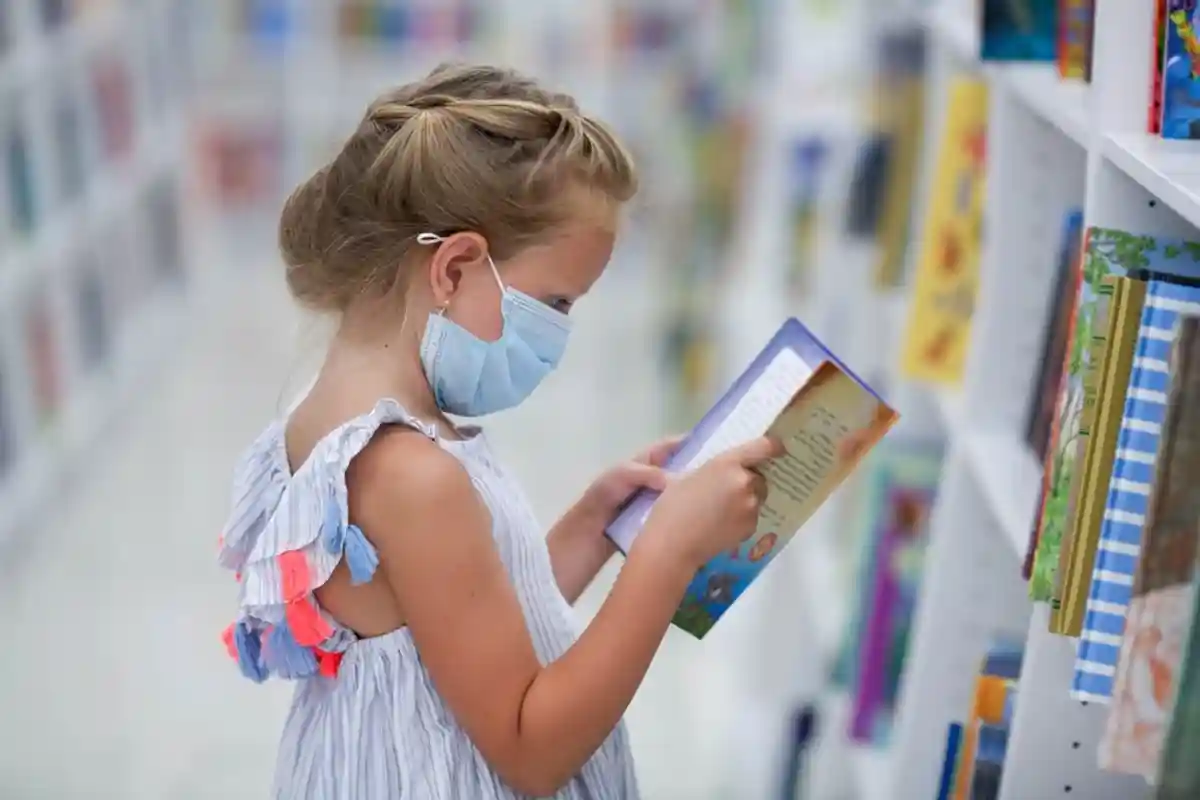 девочка в защитной маске читает книгу фото