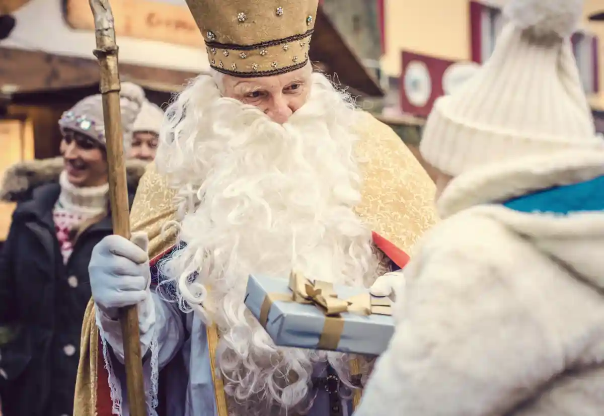 Актер в костюме святого Николая дарит детям подарки на ярмарке. Фото: Kzenon / shutterstock.com
