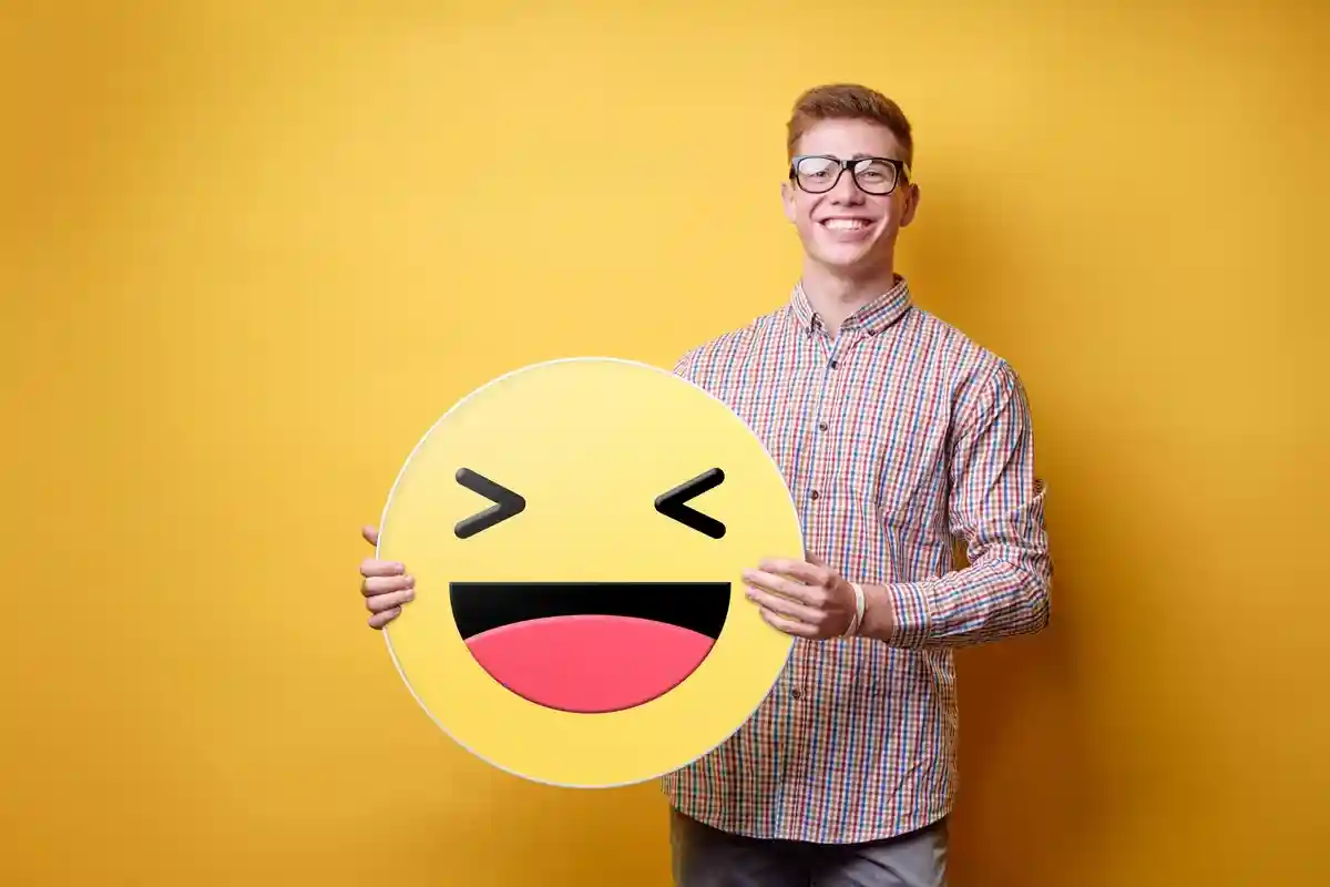 Счастливый молодой человек держит желтое смеющееся лицо эмодзи Фото: kudla/Shutterstock.com