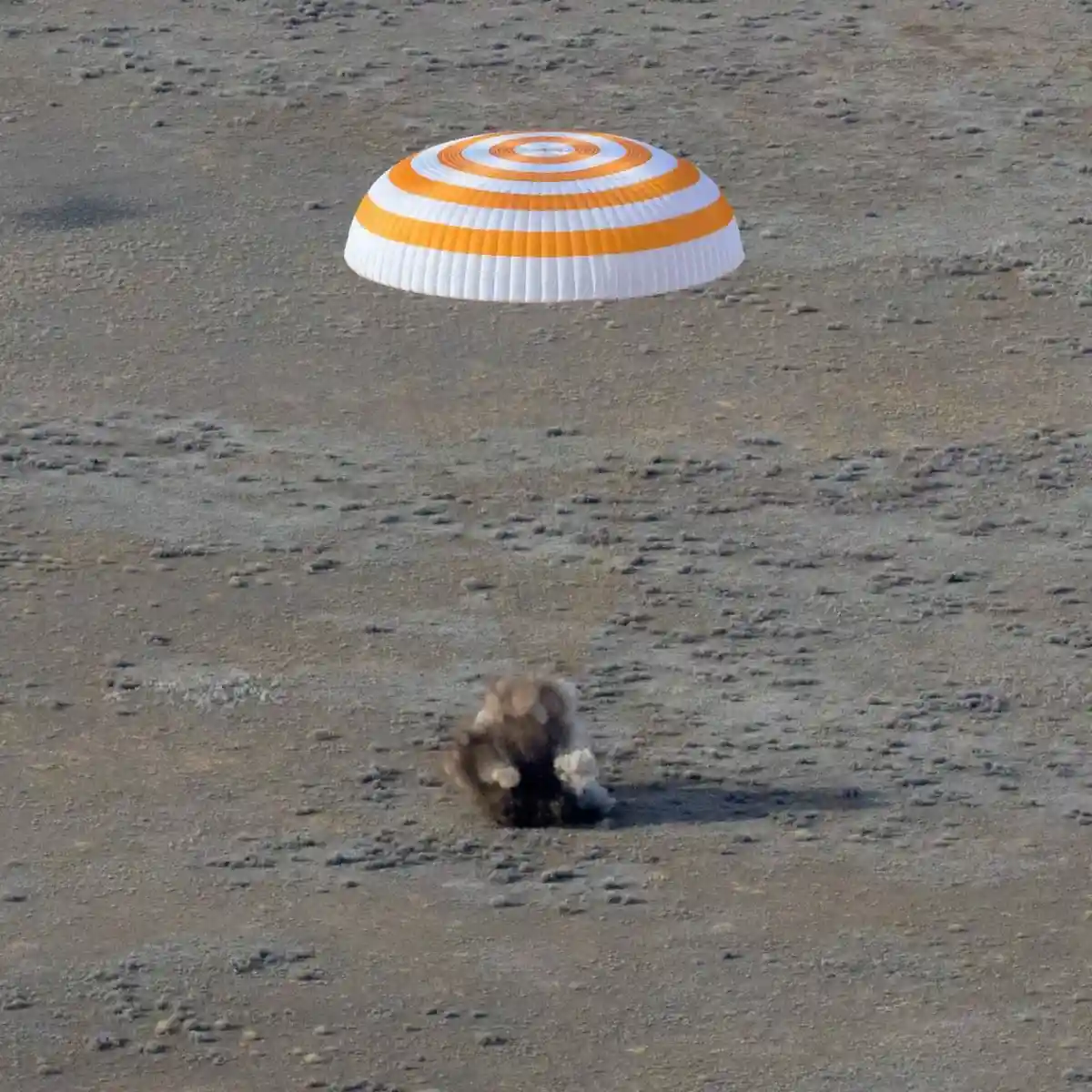 Спускаемый на оранжево-белом парашюте модуль "Союз"