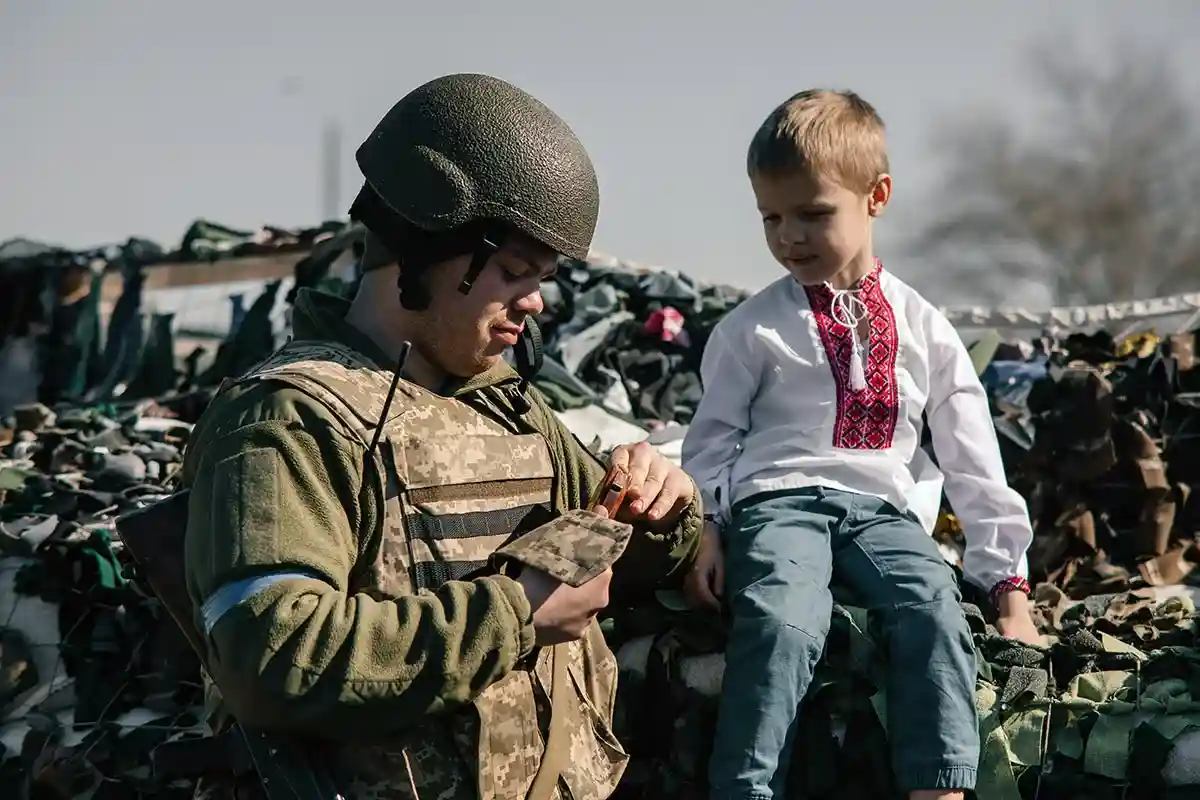 Блокпост. Мальчик сидит на мешках с песком возле воина из украинской территориальной обороны. Фото: shutterstock.com