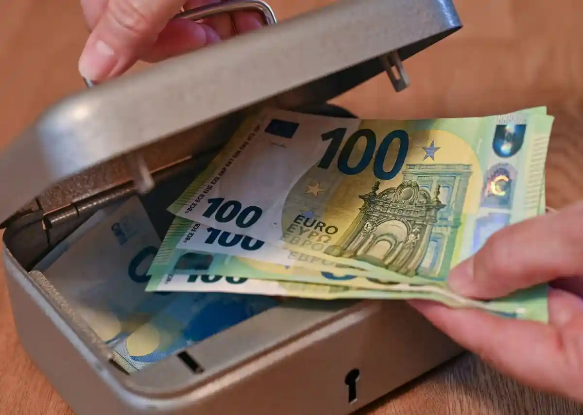 Деньги:Женщина достает банкноты евро из небольшого денежного ящика.