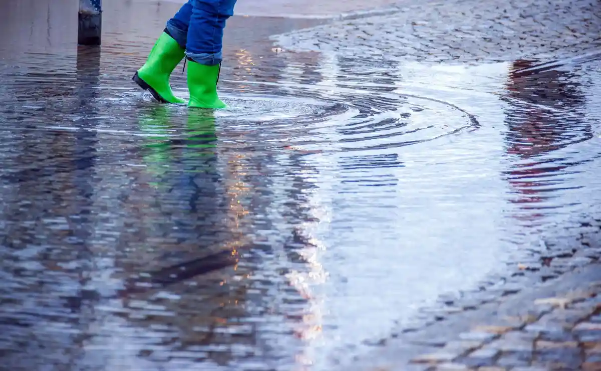 Дождливая погода:Женщина в резиновых сапогах идет по слегка затопленной улице.