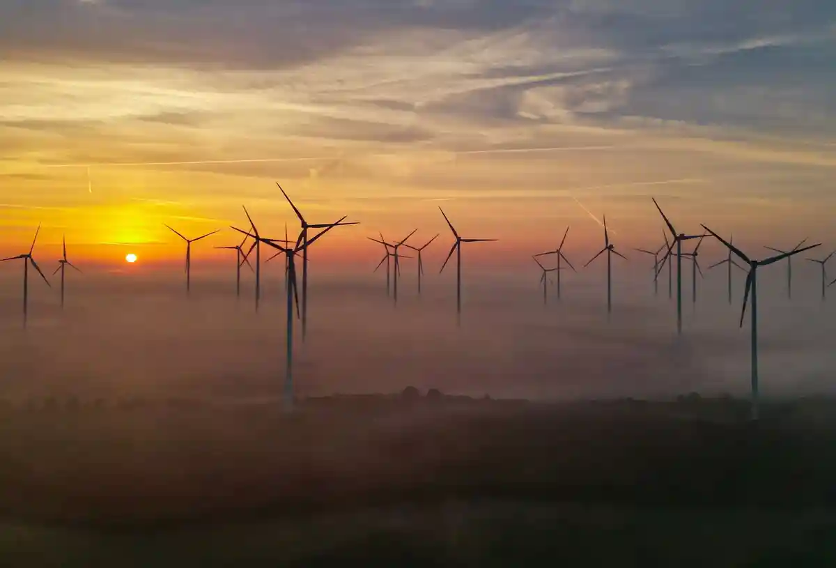 Энергия ветра:Восход солнца пробивается сквозь утренний туман над ветряной электростанцией.