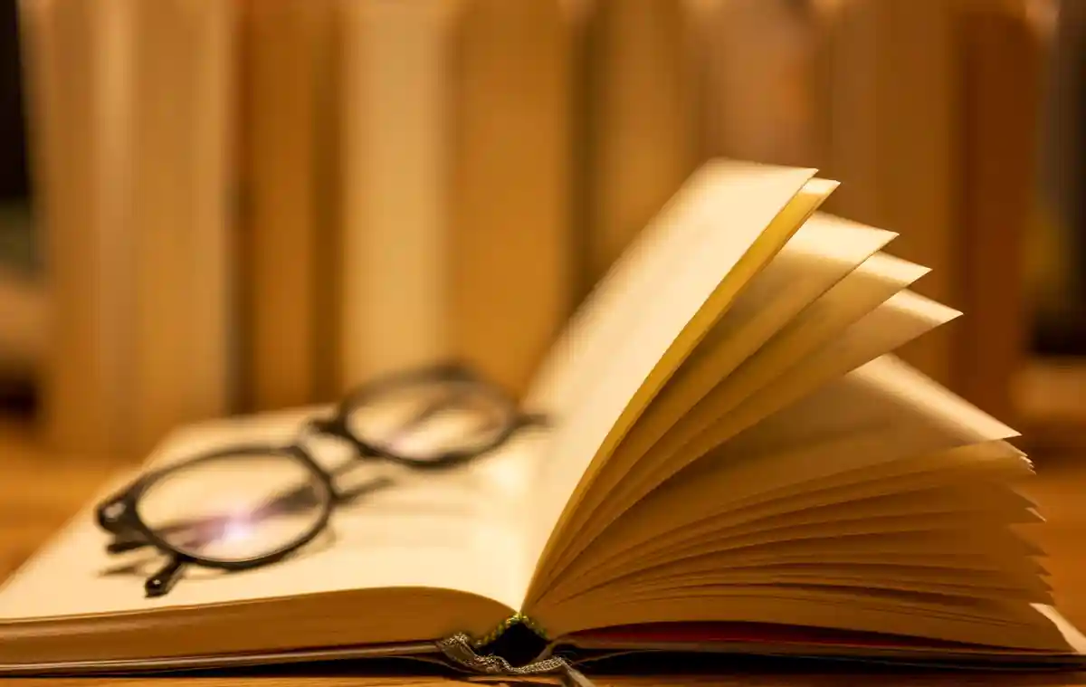 Литература:На раскрытой бумажной книге лежат очки для чтения.