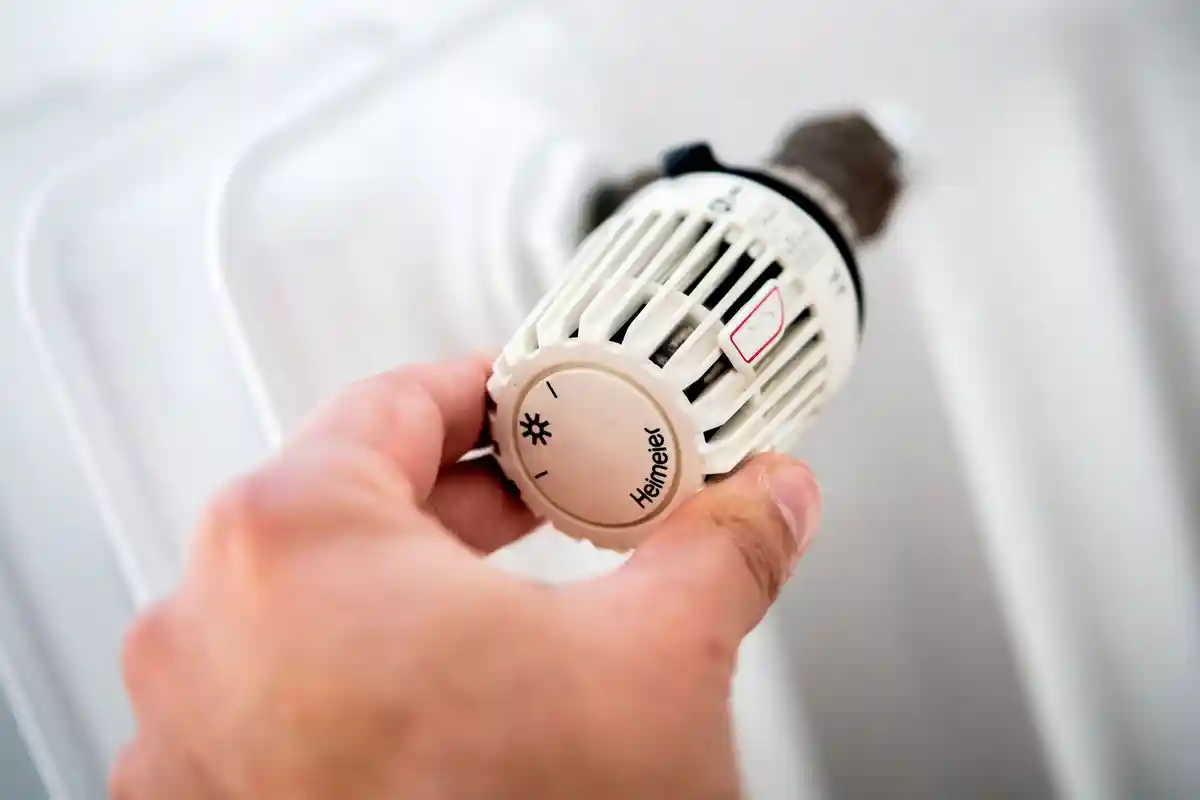 Отопление:Мужчина поворачивает термостат обогревателя в квартире.