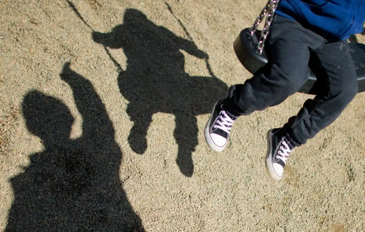 Прием несопровождаемых беженцев:Тень мужчины и качающегося ребенка на детской площадке.