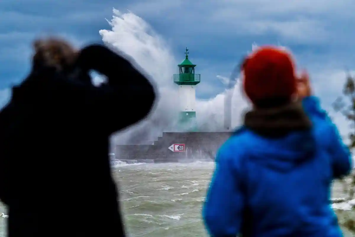Штормовой нагон на Балтийском побережье:Люди фотографируют волны Балтийского моря, бьющиеся о маяк на восточном пирсе во время сильной штормовой депрессии.