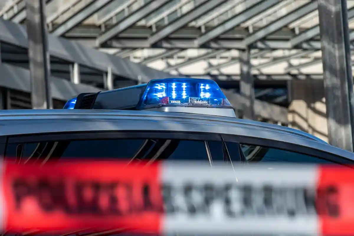Синий свет:Над заградительной лентой с надписью "Polizeiabsperrung" светит полицейский синий фонарь.