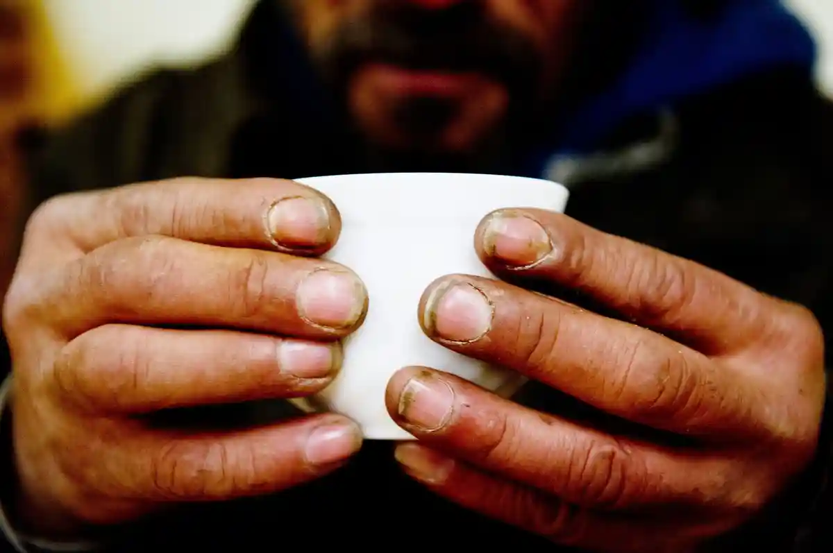 Бездомность:Бездомный держит чашку в ночном кафе.