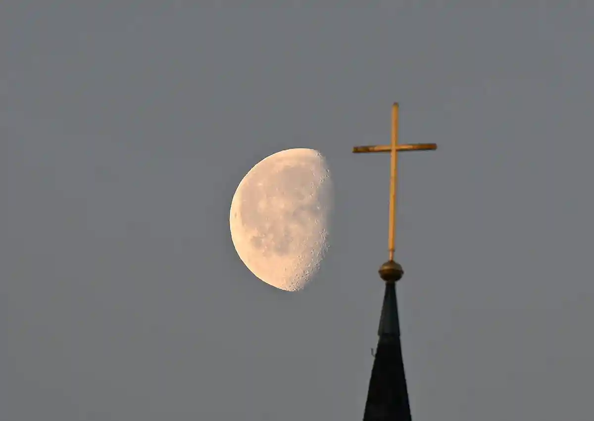 Крест на церковной башне:Луна стоит в утреннем свете за крестом на церковной башне.