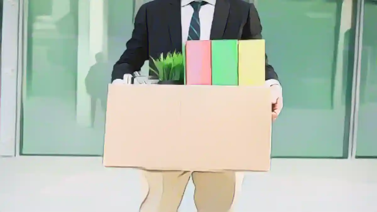 На рисунке изображен мужчина перед офисным зданием. В руках у него картонная коробка. В коробке находится растение и три разноцветные папки.:В случае увольнения работники получают определенные льготы и имеют особые права.