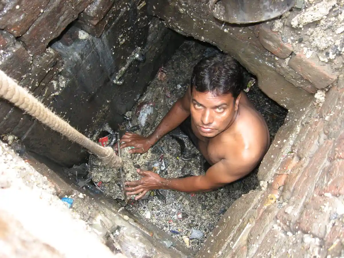 Очистка канализационных труб в Индии:Чистильщик канализации работает в канализационной системе на окраине Нью-Дели - без защитной одежды.