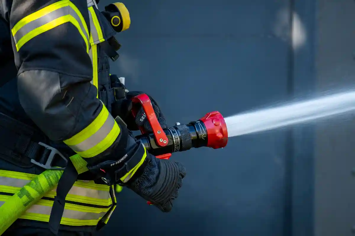 Пожарная охрана:Сотрудник пожарной бригады распыляет воду из шланга.