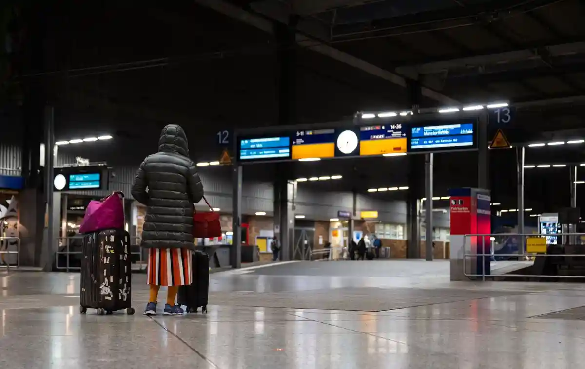 Предупредительная забастовка на железной дороге:Путешественница стоит с багажом в главном зале железнодорожного вокзала.