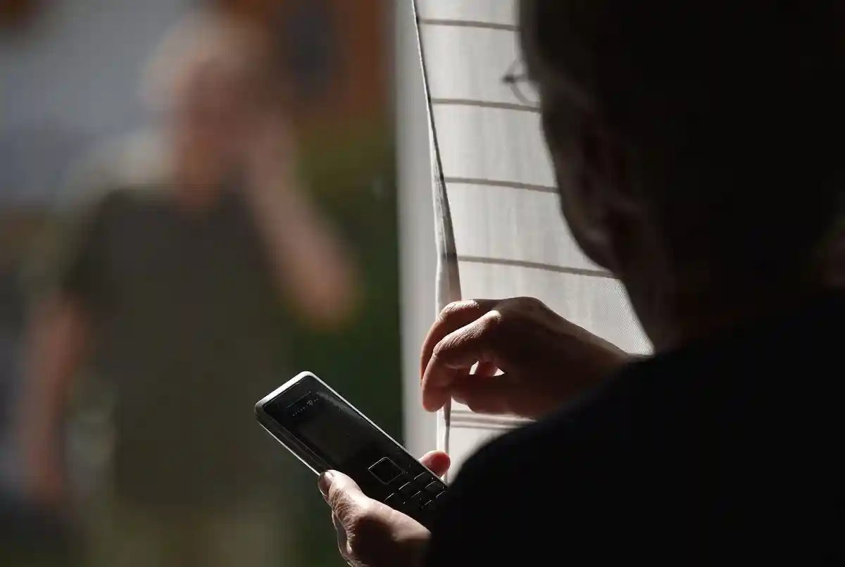 Преследование:Женщина стоит у окна с телефоном, перед которым стоит мужчина (постановочная сцена).