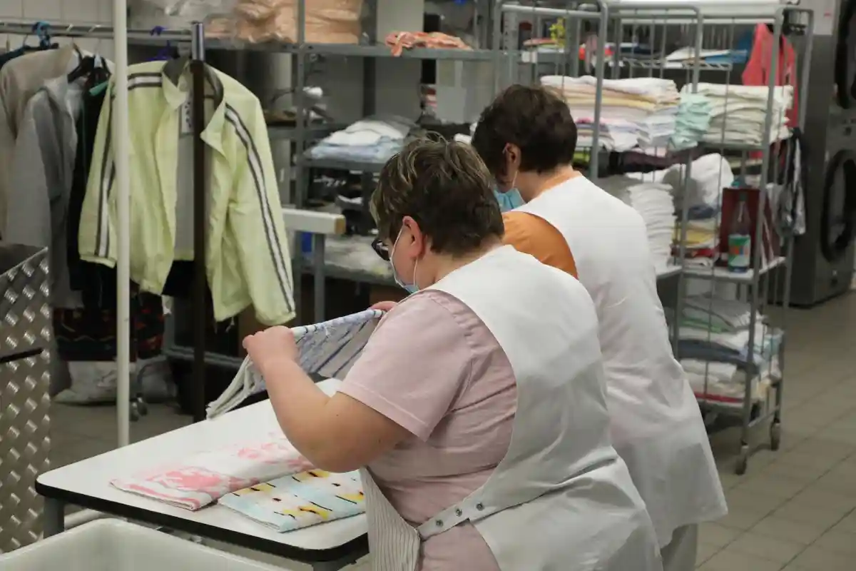 Семинары для людей с ограниченными возможностями:Две женщины работают в прачечной Lebenshilfe Gera e.V., где складывают белье.