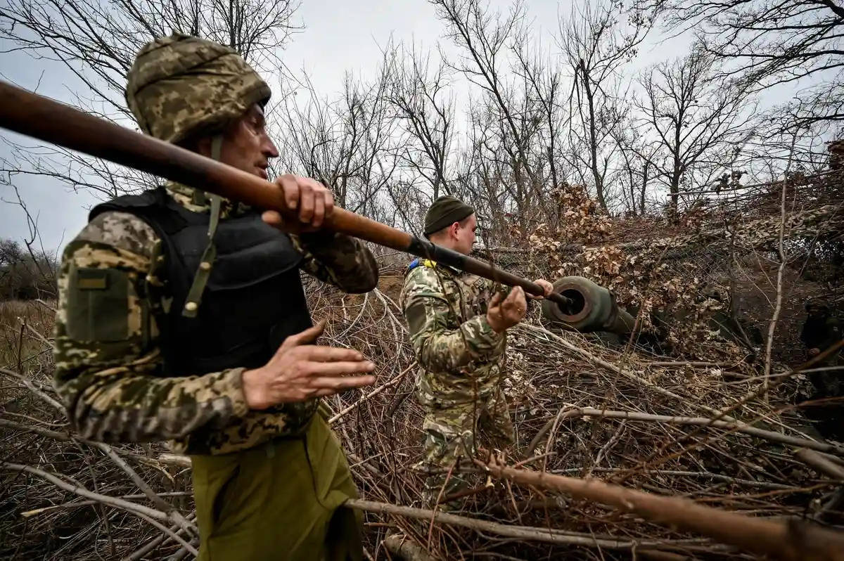Война на Украине:Два солдата чистят ствол самоходной гаубицы в камуфляжной форме.