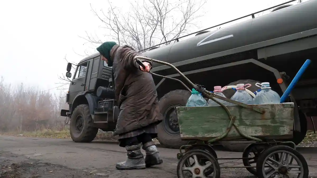 Война на Украине - Донецк:Пожилой мирный житель тянет тележку с бутылками пресной воды, которую раздает российская армия в контролируемом Россией регионе.
