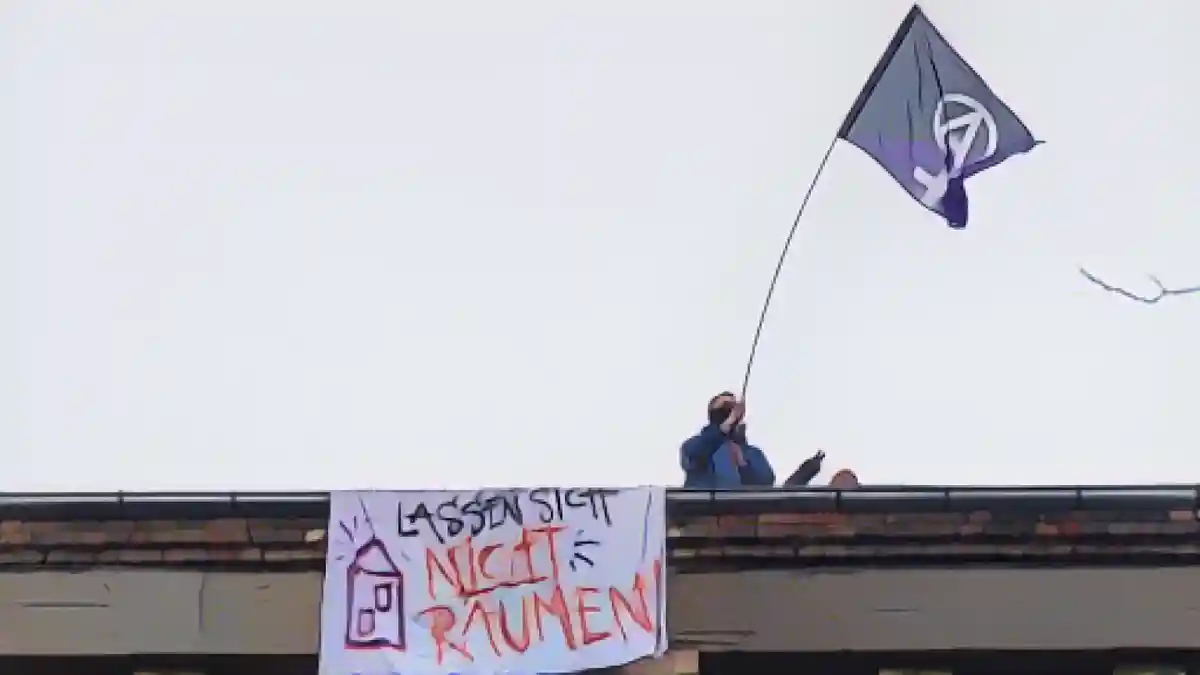 Активист стоит с флагом на крыше типографии "Дондорф" с плакатом "Не дайте им убраться".:Активист стоит с флагом на крыше типографии "Дондорф" с плакатом "Не дайте им убраться". Фото