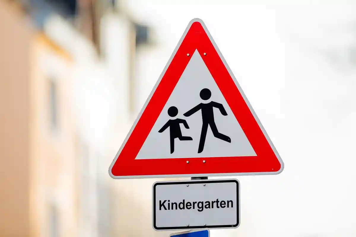 Детский сад:Дорожный знак с надписью "Детский сад" стоит перед детским садом.