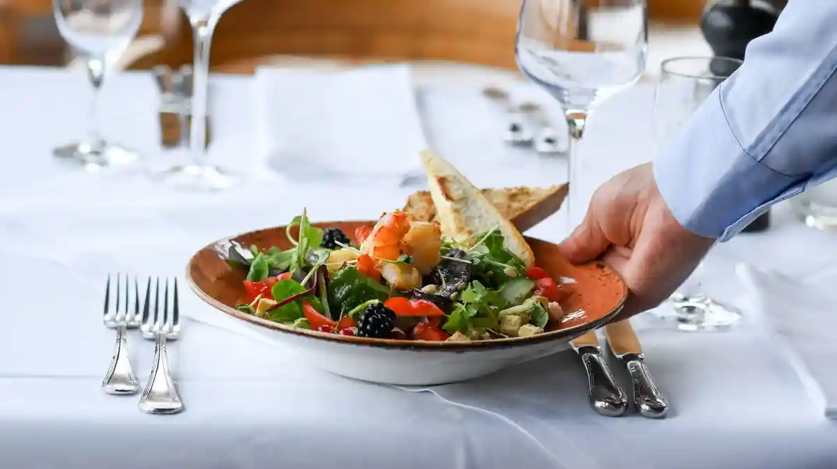 Гастрономия:Официант подает тарелку с салатом в ресторане.