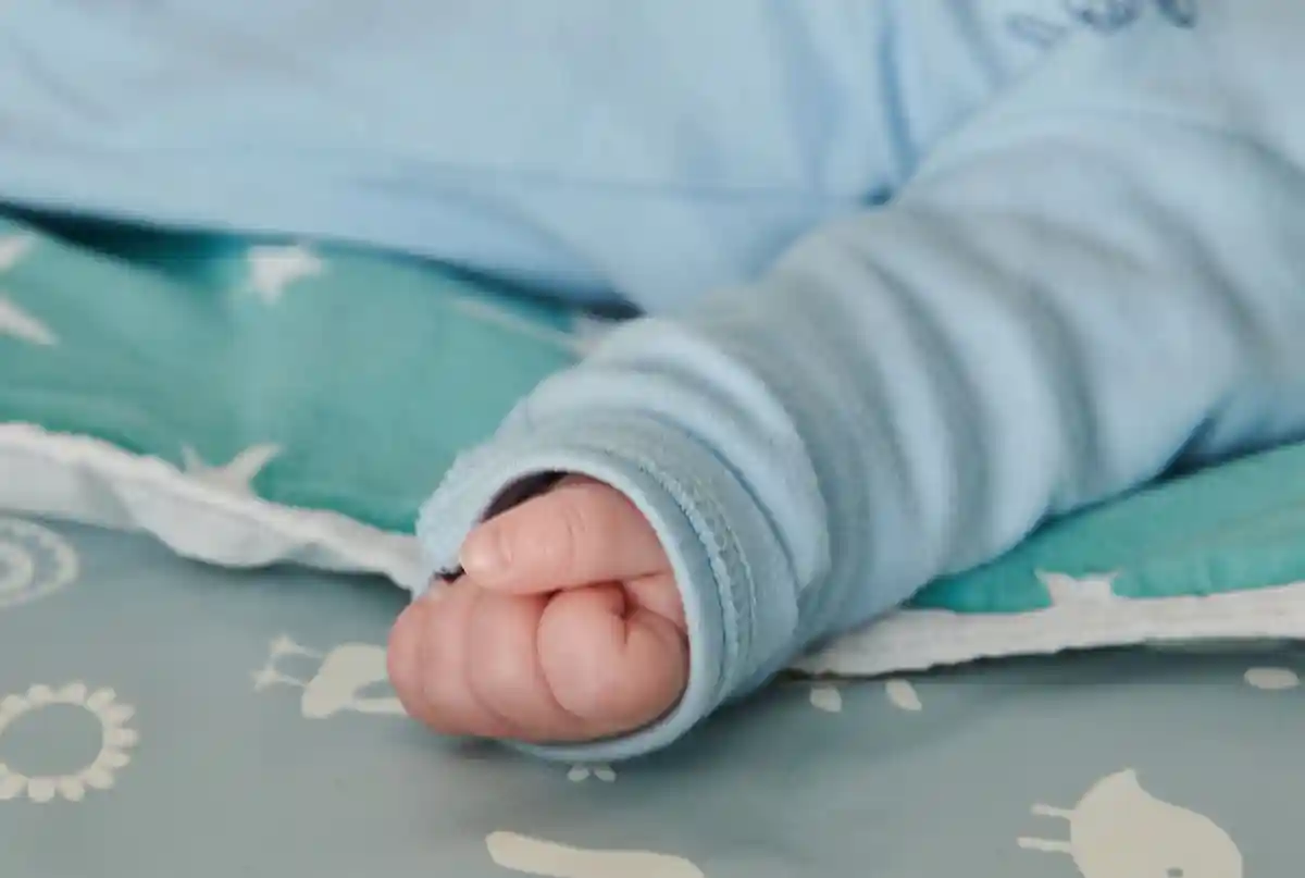Малыш:Младенец, которому всего несколько недель от роду, сжимает руку в маленький кулачок.