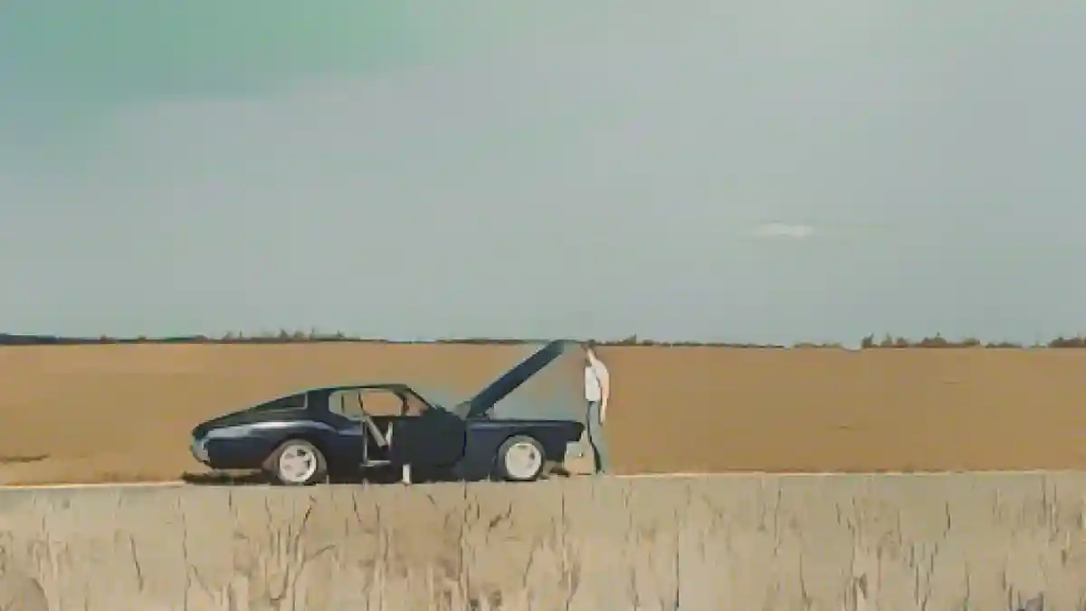 Мужчина смотрит в открытый капот ретро-автомобиля в поле:Что делать, если ваш автомобиль перегревается, по мнению механиков