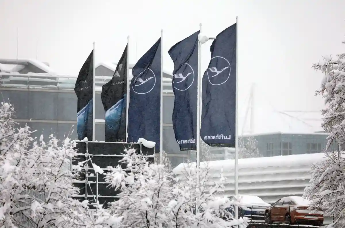 Наступление зимы на юге Германии - Мюнхен:Флаги Lufthansa развеваются в аэропорту во время снегопада.