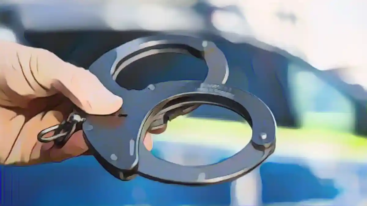 Одна рука держит наручники перед полицейской патрульной машиной.:Рука держит наручники перед полицейской патрульной машиной. Фото