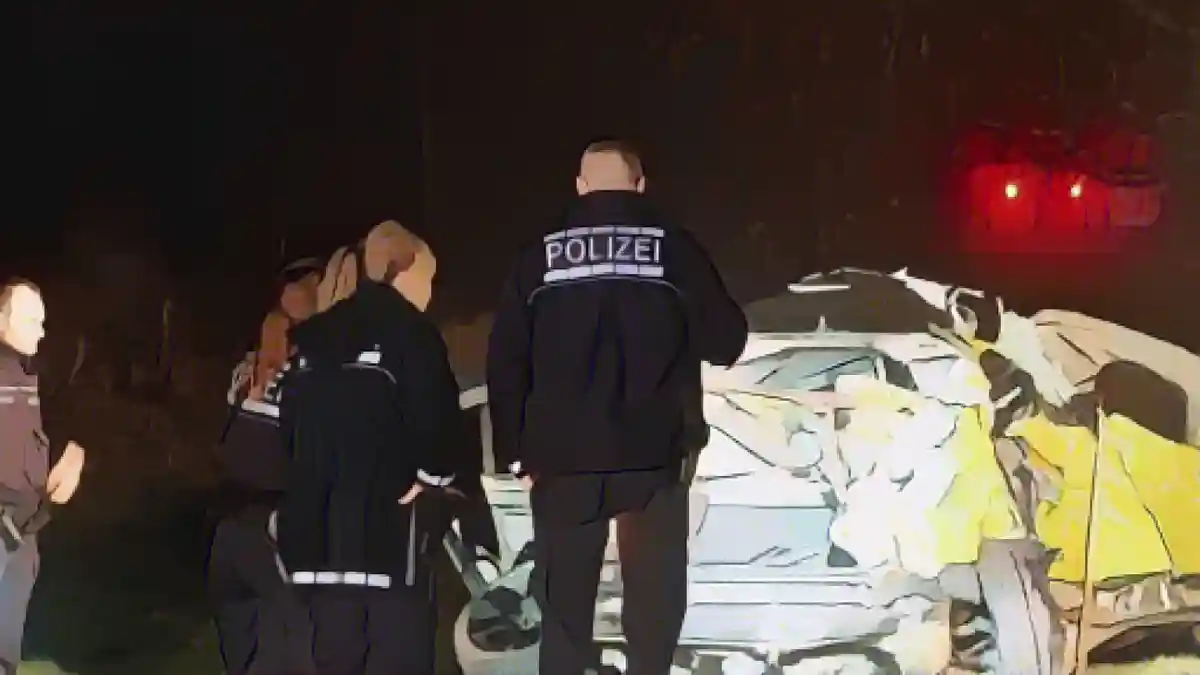Полицейские стоят перед обломками автомобиля, попавшего в аварию.:Полицейские стоят перед обломками автомобиля, попавшего в аварию. Фото