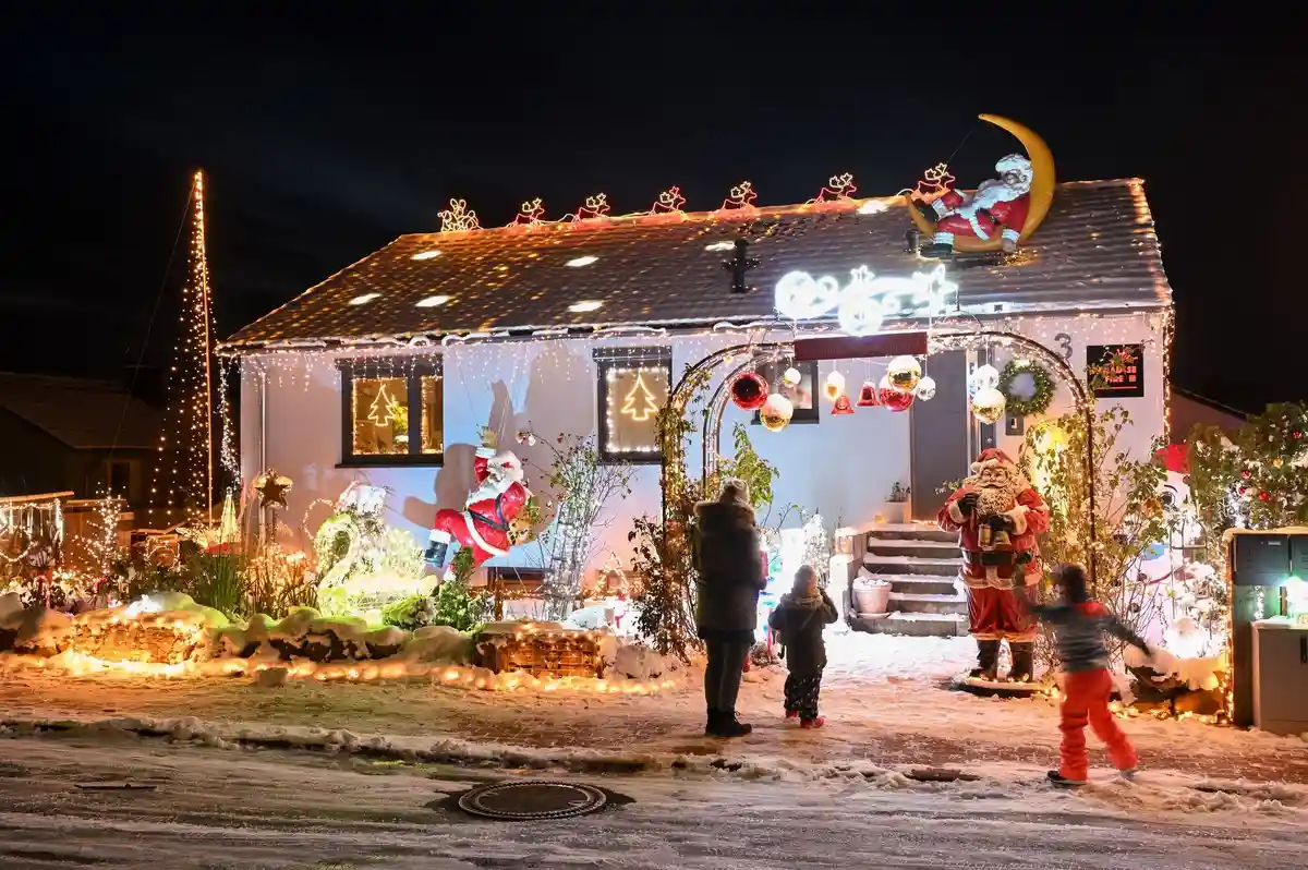 Рождественский дом - Гессен:Женщина с двумя детьми стоит перед освещенным рождественским домом.