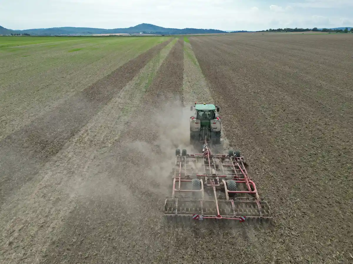 Сельское хозяйство:Трактор рыхлит почву на поле бороной, поднимая при этом облако пыли.