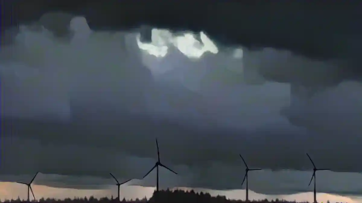 Ветряные турбины стоят под густыми дождевыми облаками за лесом.:Ветряные турбины стоят под плотными дождевыми облаками за лесом. Фото