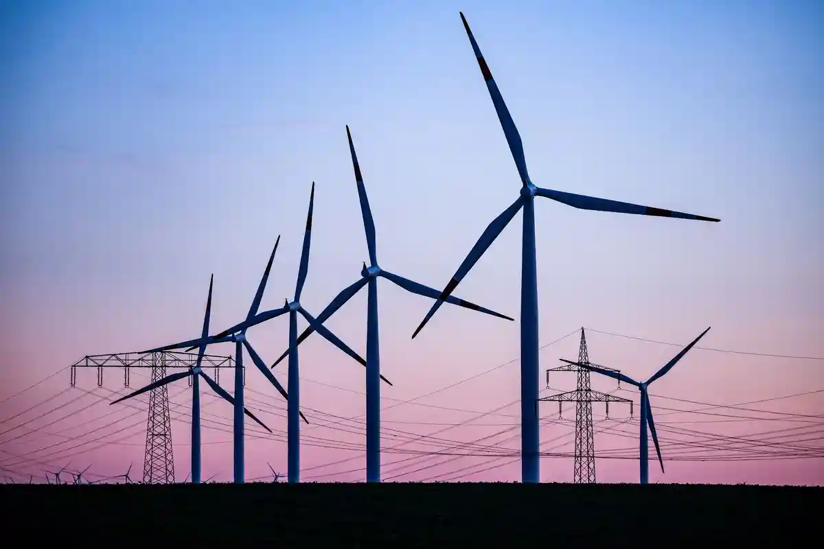 Ветряные турбины за линиями электропередач:На фоне вечернего неба видны ветряные турбины и высоковольтные линии электропередач.