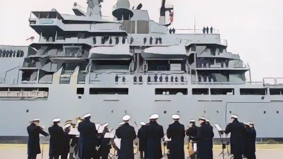 Военно-морской музыкальный корпус Вильгельмсхафена стоит на причальной стенке, в то время как "Франкфурт-на-Майне" заходит в гавань.:Военно-морской музыкальный корпус Вильгельмсхафена стоит на причальной стенке во время захода судна "Франкфурт-на-Майне" в гавань. Фото