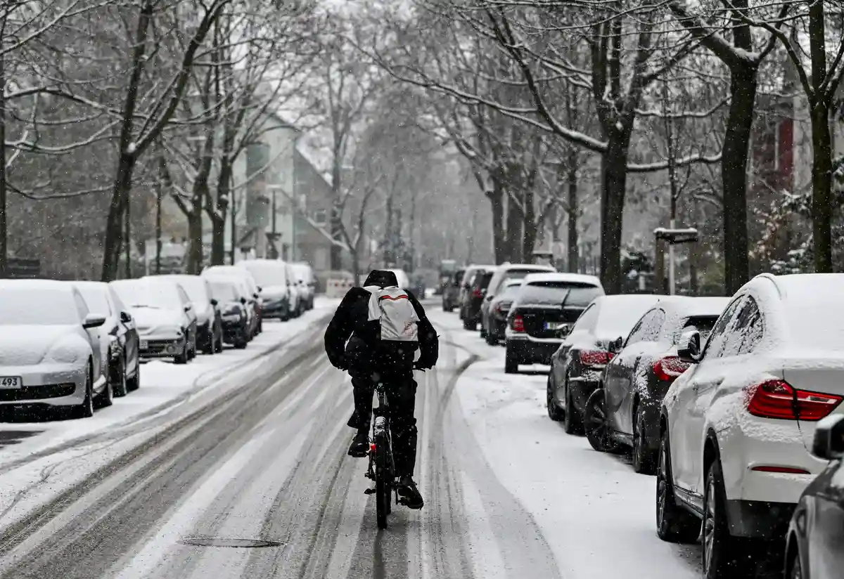 Зимняя погода - Берлин:Велосипедист едет по заснеженной дороге в Карлсхорсте, на которой видны следы автомобилей.
